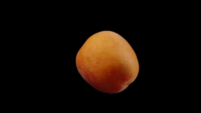 An apricot on a black background rotates in close-up, isolated.