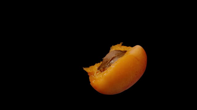 A half-eaten apricot with a pit on a black background rotates slowly in close-up, isolated.