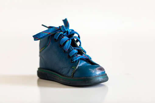 Worn out kiddie-size blue lace-ups. Isolated on white background with shadow reflection. Children's shoes with laces. Small baby's booties on reflective underlay. Old ankle boots for small kid.