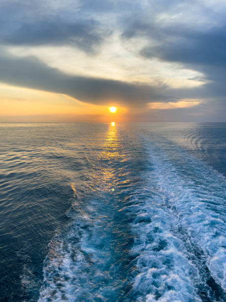 istock Ship trails on blue sea. Sun setting on horizon vertical image 1680420853
