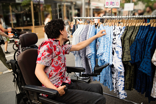 Young man with cerebral palsy shopping in city street. He is from indonesian ethnicity and a member of the LGBTQ community. He is using a wheelchair. Horizontal waist up outdoors shot with copy space. This was taken in Montreal, Quebec, Canada.