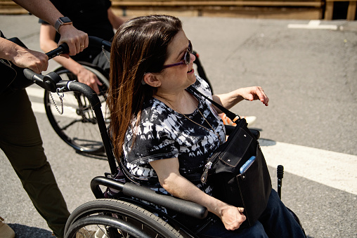 Woman living with disabilities strolling in city street. She is caucasian woman wearing sunglasses. She is using a wheelchair. Horizontal waist up outdoors shot with copy space. This was taken in Montreal, Quebec, Canada.