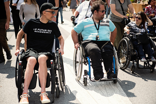 Friends living with disabilities strolling in city street. They all are using wheelchairs, manifesting for more accessibility in the city. Horizontal full length outdoors shot with copy space. This was taken in Montreal, Quebec, Canada.