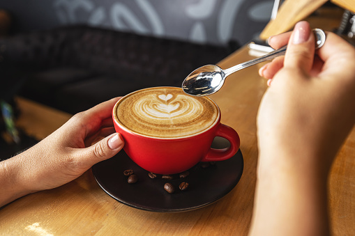 Hands of woman holding cup of cappuccino with coffee art
