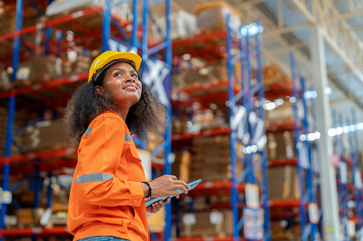 African American worker in distributor warehouse using digital tablet and walking to inspect and controlling stock inventory. Ensures that products are readily available for distribution, contributing to a smooth supply chain operation and customer satisfaction.