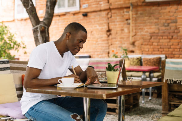Serious, concentrated and enthusiastic afro american man using laptop and drinking coffee in internet cafe. Do business