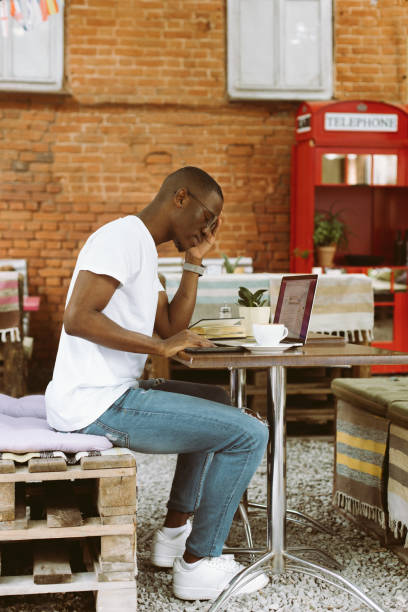 istock Vertical multicultural businessman with laptop, phone in coffee shop, hold head with hand, work online as self-employed 1680449856