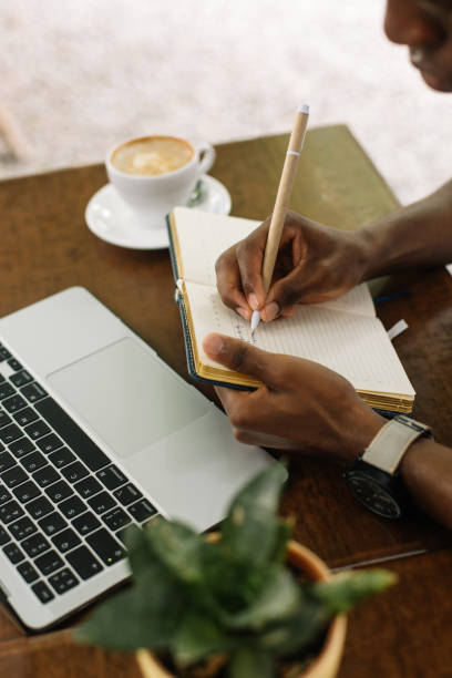istock Vertical cropped multiracial businessman using laptop, taking notes in workbook, drink coffee in street cafe. High angle 1680449865