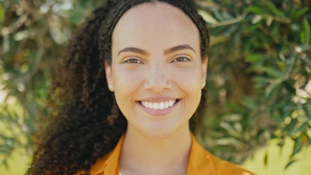 Close-up video portrait of gorgeous hispanic or brazilian curly woman, stand outdoors, looking at camera with charming cute toothy smile, posing in casual stylish wear. Female student or freelancer