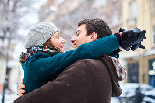 Embracing couple in love kissing in winter park. Cheerful loving man and woman are hugging while spending winter holidays together