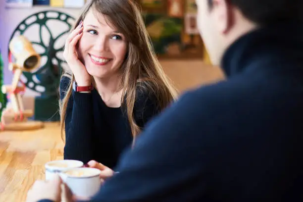 Photo of loving couple sitting in little bistro in winter and drink hot tea and coffee. focus on woman face in background