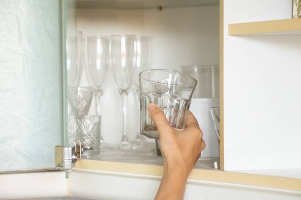 la main d’une femme prend un verre d’une étagère dans une armoire de cuisine dans un appartement, prend un verre - placard holding celebration women photos et images de collection