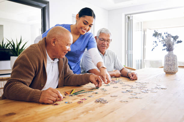 puzzle, caregiver and senior men playing a game as entertainment or bonding together in a retirement home. happy, fun and elderly people enjoy mental rehabilitation and development with nurse - ouderenzorg stockfoto's en -beelden