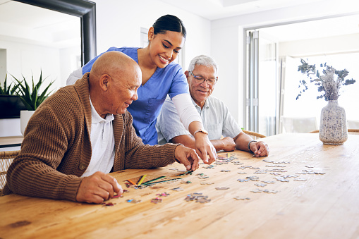 Puzzle, caregiver and senior men playing a game as entertainment or bonding together in a retirement home. Happy, fun and elderly people enjoy mental rehabilitation and development with nurse