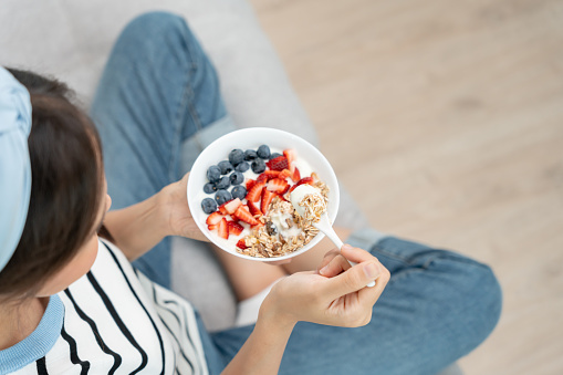 Asian Woman having delicious healthy breakfast at home on morning. Health care female eats yogurt with granola and berry fruit. Healthy food, Vitamins, clean diet, dieting, detox, organic food.