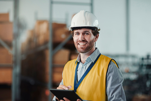 Warehouse, tablet of engineer and portrait of happy man in helmet for safety. Technology, face of worker in factory and hard hat of technician, professional architect and Industry expert in Australia