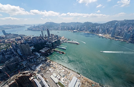 Aerial panorama of Hong Kong & Kowloon ( Tsim Sha Tsui ) with crowded modern skyscrapers by Victoria Harbour & ships navigating across the busy seaport ~ Beautiful cityscape of Hongkong on a sunny day