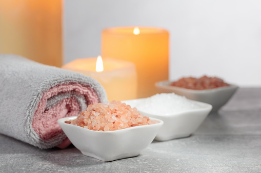 Sea salt, towels, and burning candles on a grey background. Spa concept with copy space.