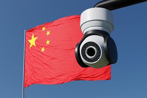 Surveillance camera in public area in front of the national flag of China under blue sky. Illustration of the concept of mass surveillance