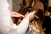 Hairdresser's hands prepare brown hair for dyeing with a comb and foil in a beauty salon, close up.