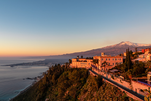 Luxury San Domenico Palace Hotel with panoramic view on snow capped Mount Etna volcano at sunrise from public garden Villa Comunale in Taormina, Sicily, Italy, Europe, EU. Coastline Mediterranean sea