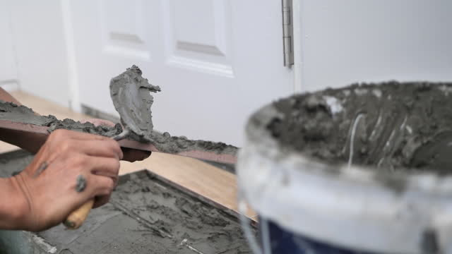 Close-up of professional repairman placing liquid cement on the floor of construction.