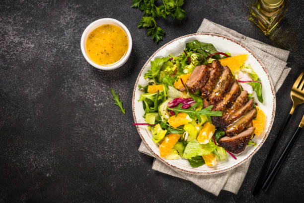 Salad with baked duck, green salad mix and oranges. Salad with baked duck, green salad mix and oranges and honey mustard dressing. Healthy food, diet meal. Top view at black stone table. mustard fruits stock pictures, royalty-free photos & images