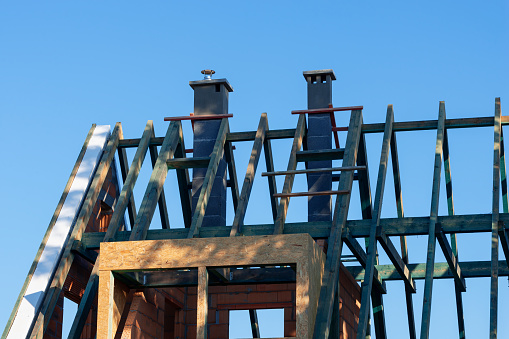 Wooden roof structure and chimneys on unfinished detached house against blue sky