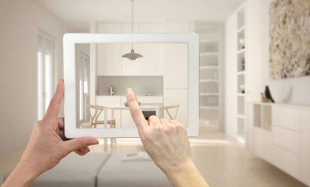 istock Hands holding and pointing on tablet showing modern kitchen. Blurry minimalist white kitchen in the background, architecture interior design presentation 1680692671
