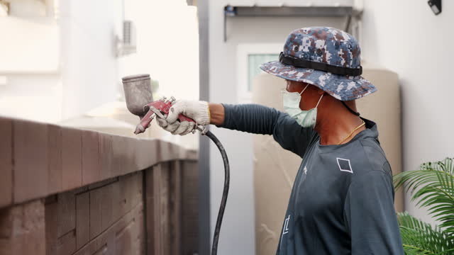 Asian worker wearing workwear painting the wall by airless spray gun. Airless spray painting.
