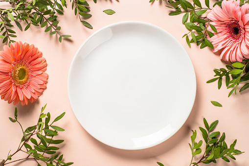 Table setting with white plate, flowers and cutlery at pink background. Top view with copy space.