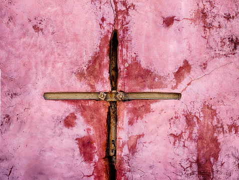 An iron brace on a pink wall intended to stabilize a crack in the town of Oia takes on the shape of a cross.