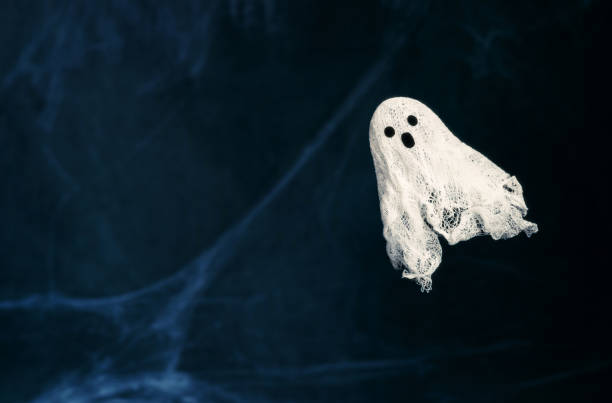 Halloween background with ghost and spider web. Ghost made of gauze on a dark blue background with copy space. Creative DIY Halloween decor.