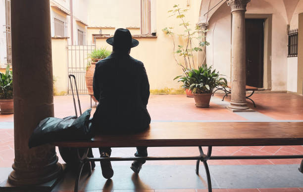 Gentleman dressed in old fashion waits patiently. Back view of an artist with his suitcase in an ancient hall. Italian style, travel and tourism. Musician in silhouette