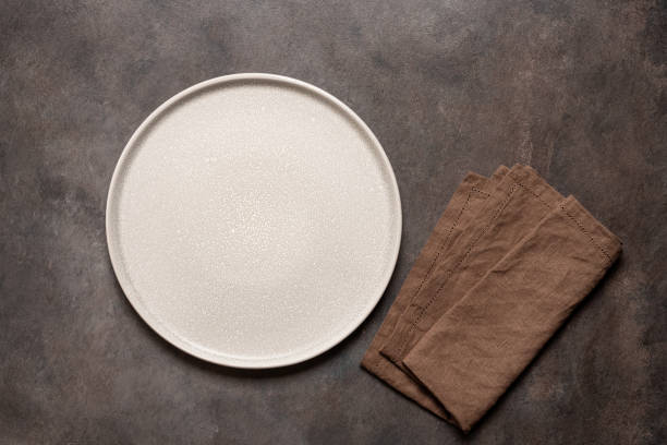 istock Empty beige plate with brown linen napkin on brown rustic background. Top view, flat lay. 1680795805