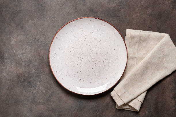 istock Empty white plate with a beige linen napkin on a brown rustic background. Top view, flat lay, copy space. 1680800686