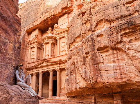 Blonde tourist woman with hat and sunglasses in Al Khazneh (The Treasury), ancient city of Petra. Historical and archaeological city in southern Jordan. Travel destinations
