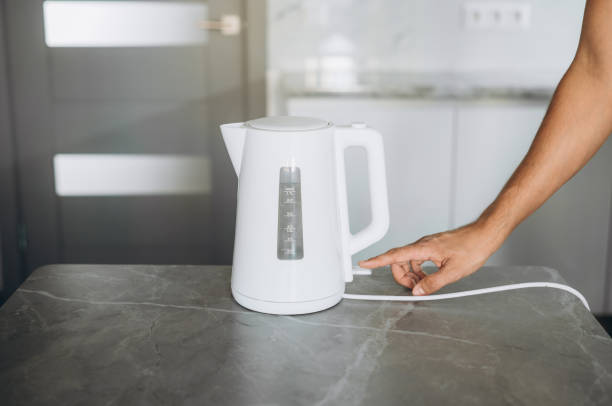 istock Male hands pouring water from a white electric kettle into a mug for making tea 1680904877