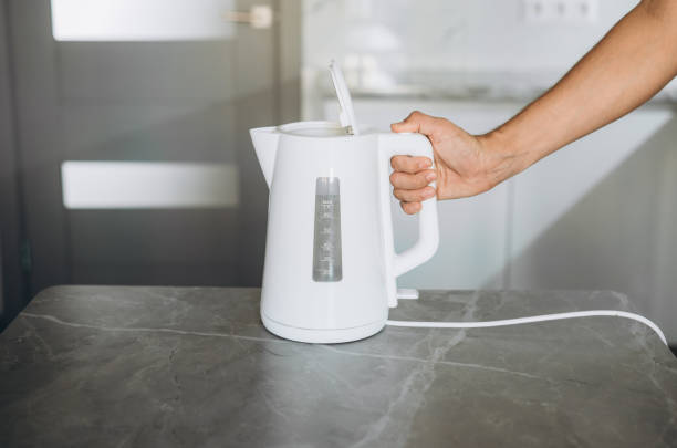istock Male hands pouring water from a white electric kettle into a mug for making tea 1680904878