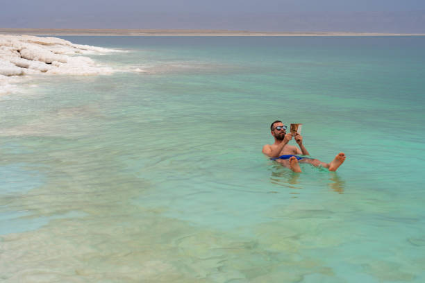 istock Relaxing tourist man reading a book while taking a bath in floating Death Sea, Jordan 1680918696