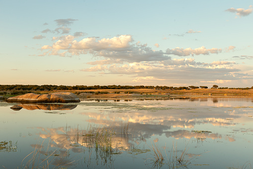 Landscape of lake in Extremadura, Spain, with reflection of clouds from sky in water. There is rock on left side. Water is very calm.