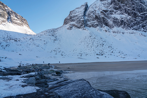 View on Kvalvika Beach, frozen rocks at the sea in winter. Some unrecognizable person at the beach. Close to the Moskensoynear fishing village Fredvang on the Lofoten Islands. Norway.