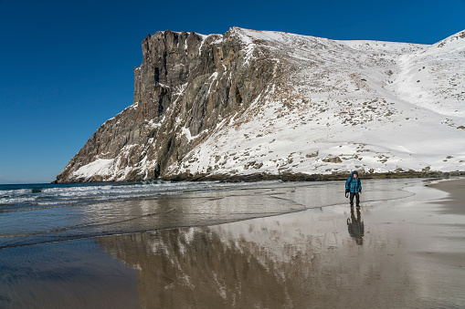 Man walking on the Kvalvika Beach, reflecting in the sea man and mountain in winter. Close to the Moskensoynear fishing village Fredvang on the Lofoten Islands. Norway.