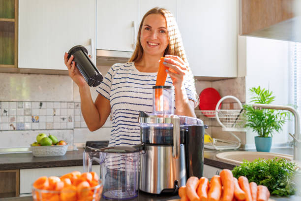 istock Young woman making carrot juice with juice machine at home kitchen 1681007027