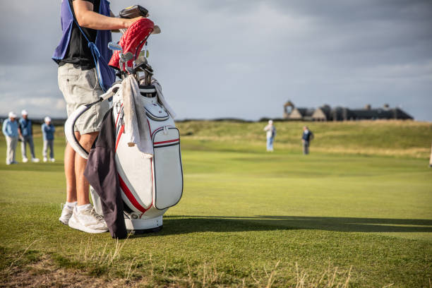 Caddy minding a golfers golf bag - with a full set of clubs, located near the green awaiting to putt. stock photo