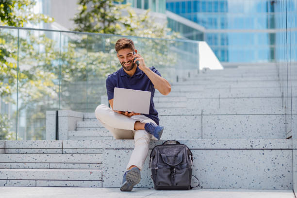 istock Smiling freelancer talking phone with client sitting with laptop on modern city background 1681024523
