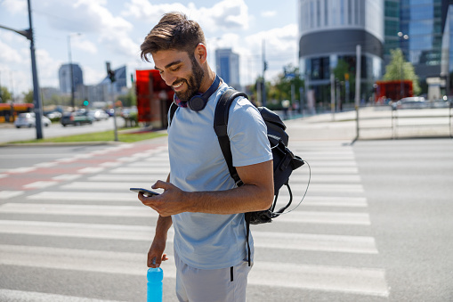 Man with phone and bottle of water standing on skyscrapers background after training and looks away