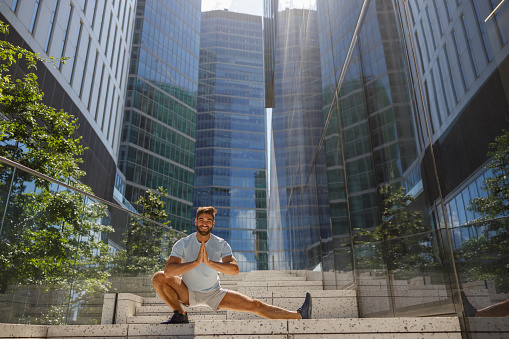 Healthy sporty man doing stretch on modern city skyscrapers background. High quality photo