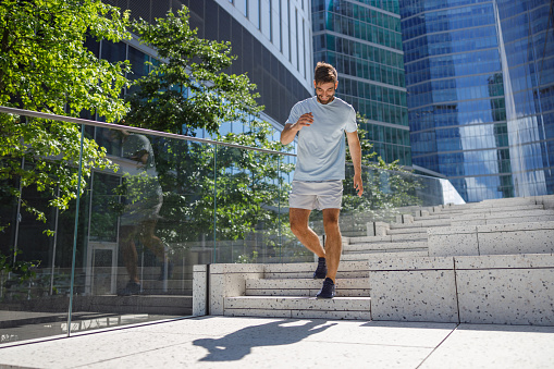 Muscular sport male sprinter in sportswear running on stairs on skyscrapers background