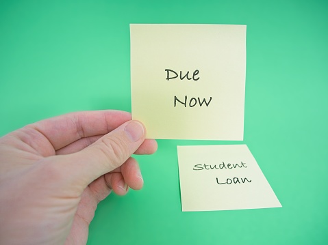 One more bill, a hand holds a sticky note with the message of student loans are now due. Hand holds note with green background and room for copy.